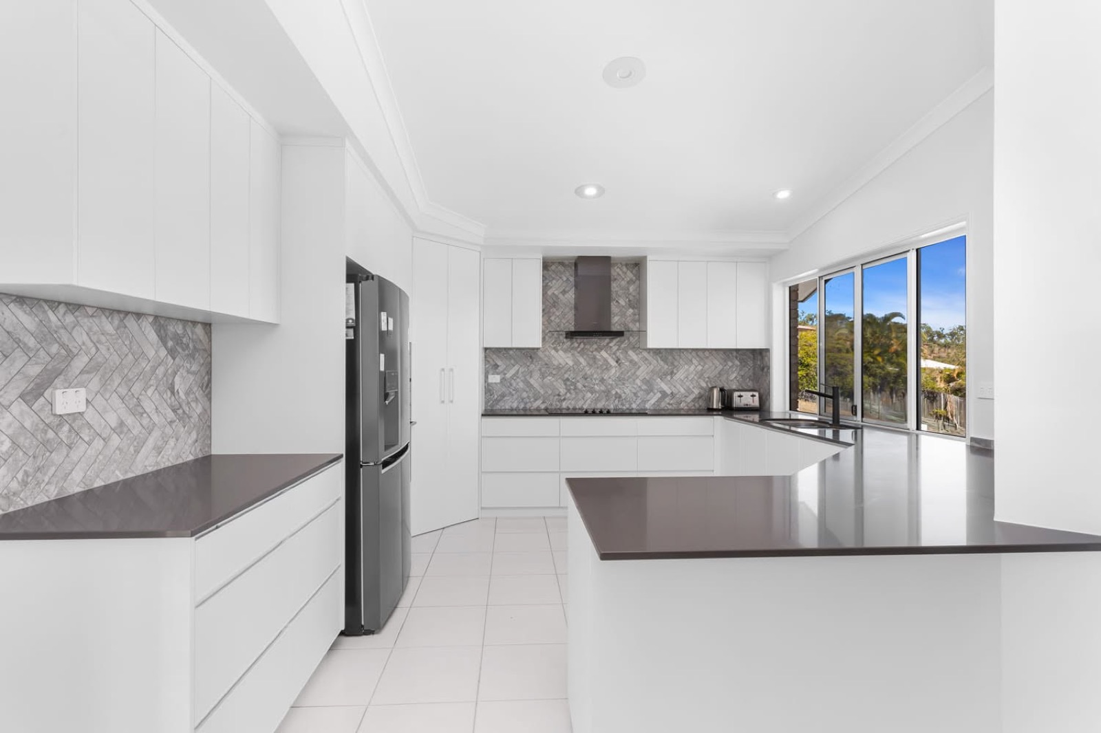 A white kitchen with grey benchtops and a herringbone tiled splashback