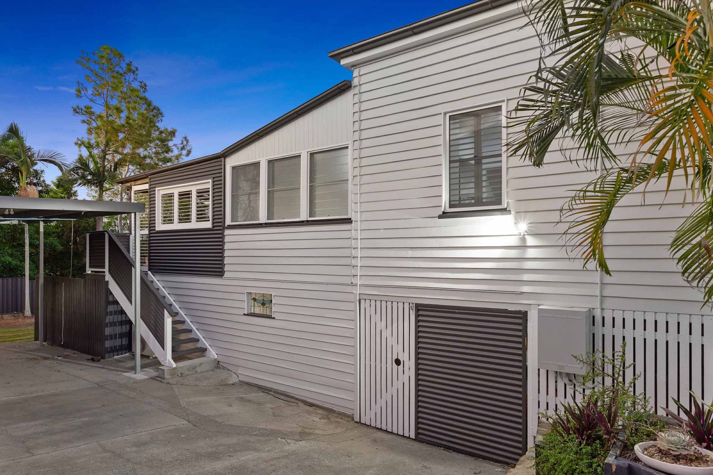 A white home with a low roofline and palms across the front garden