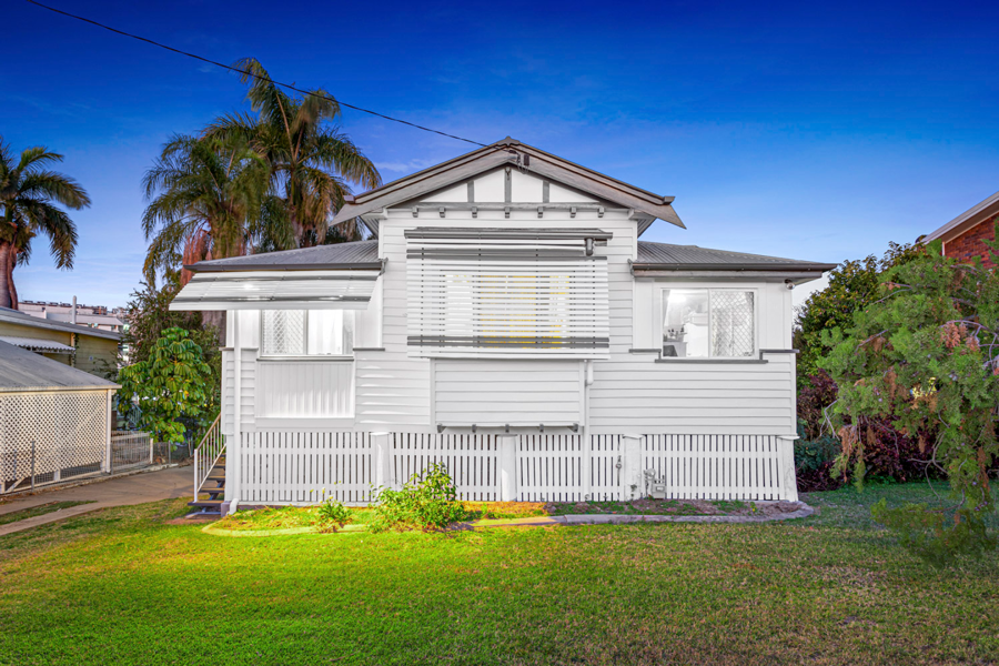A white weatherboard Queenslander with a freshly painted verandah at dusk