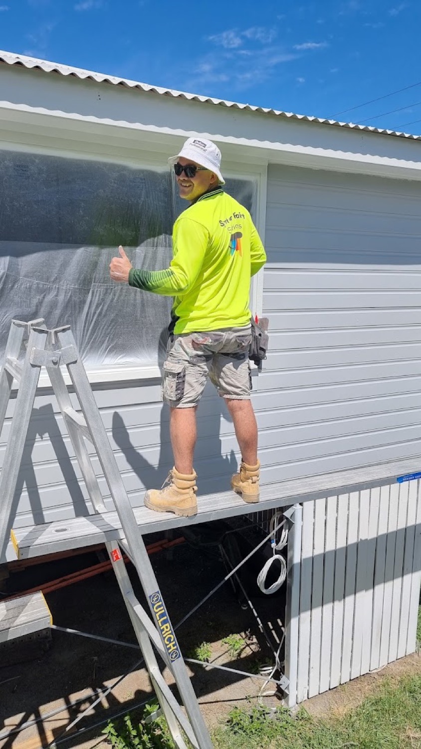 A painter in a branded shirt and hat working from a plank against weatherboard cladding