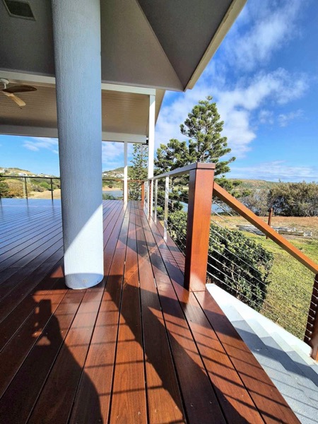 A timber deck under a white column with a coated handrail and cable balustrade