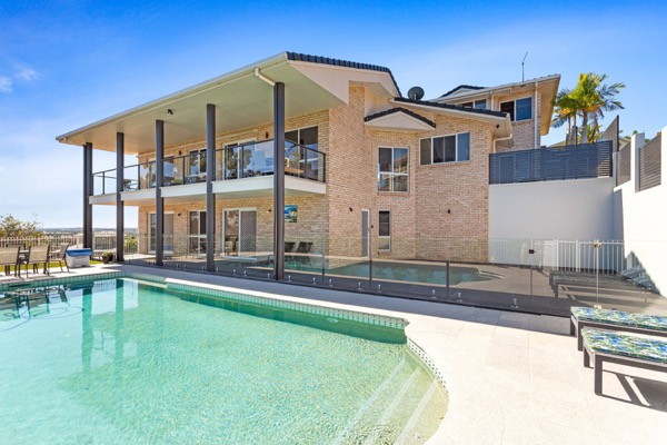 A rendered two storey home beside a swimming pool under a clear sky