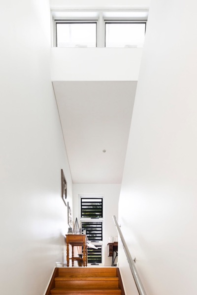 A tall white stairwell with a timber tread staircase and high windows