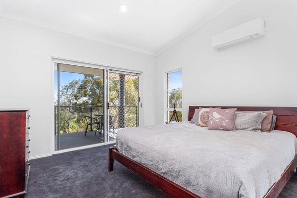 A bedroom in soft white with a sliding door out to the trees
