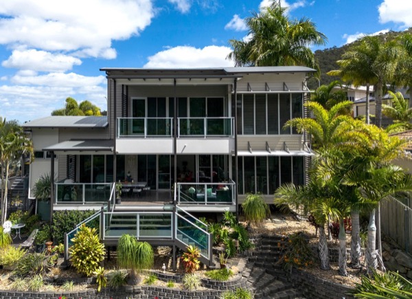 A two storey home with dark cladding and palms across the frontage
