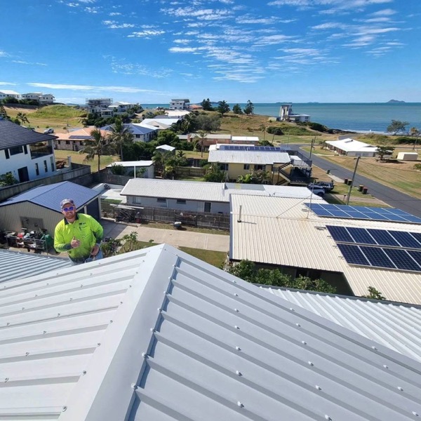 A painter in hi vis on a freshly coated metal roof with the bay behind