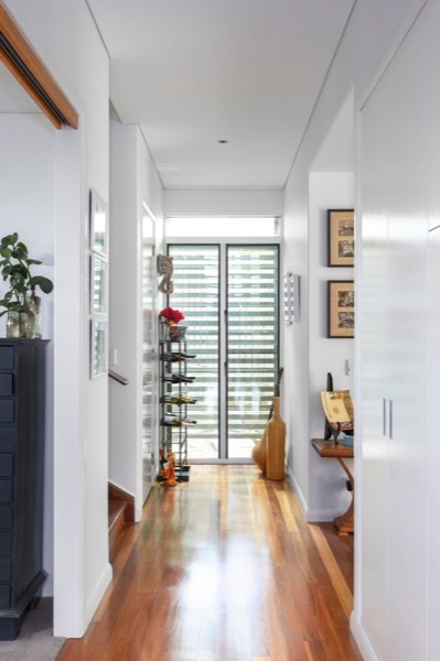 A white hallway with timber flooring and louvre windows at the far end