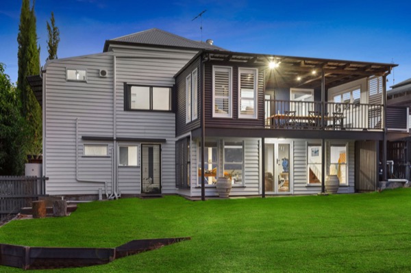 A grey two storey home at dusk with a wide upper deck and a mown lawn