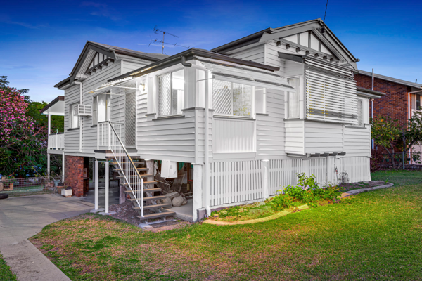 A white Queenslander with a fretwork gable and a painted front fence