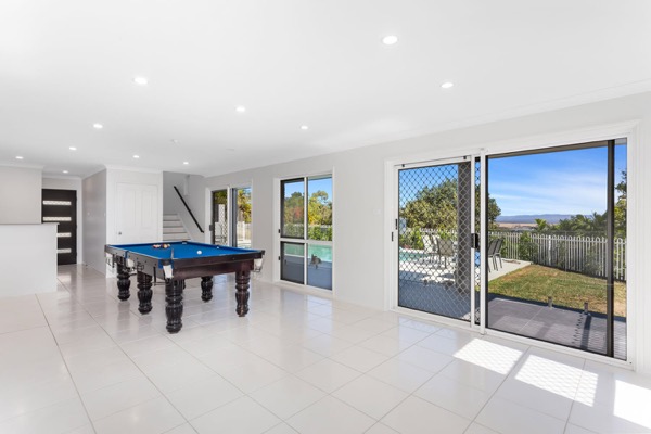 A large room in white with a pool table and glass doors to the yard