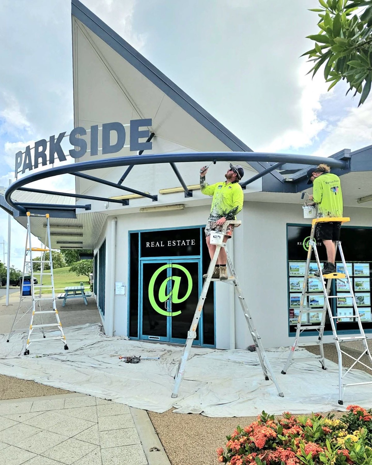 Two painters on ladders coating the curved awning of a shopfront